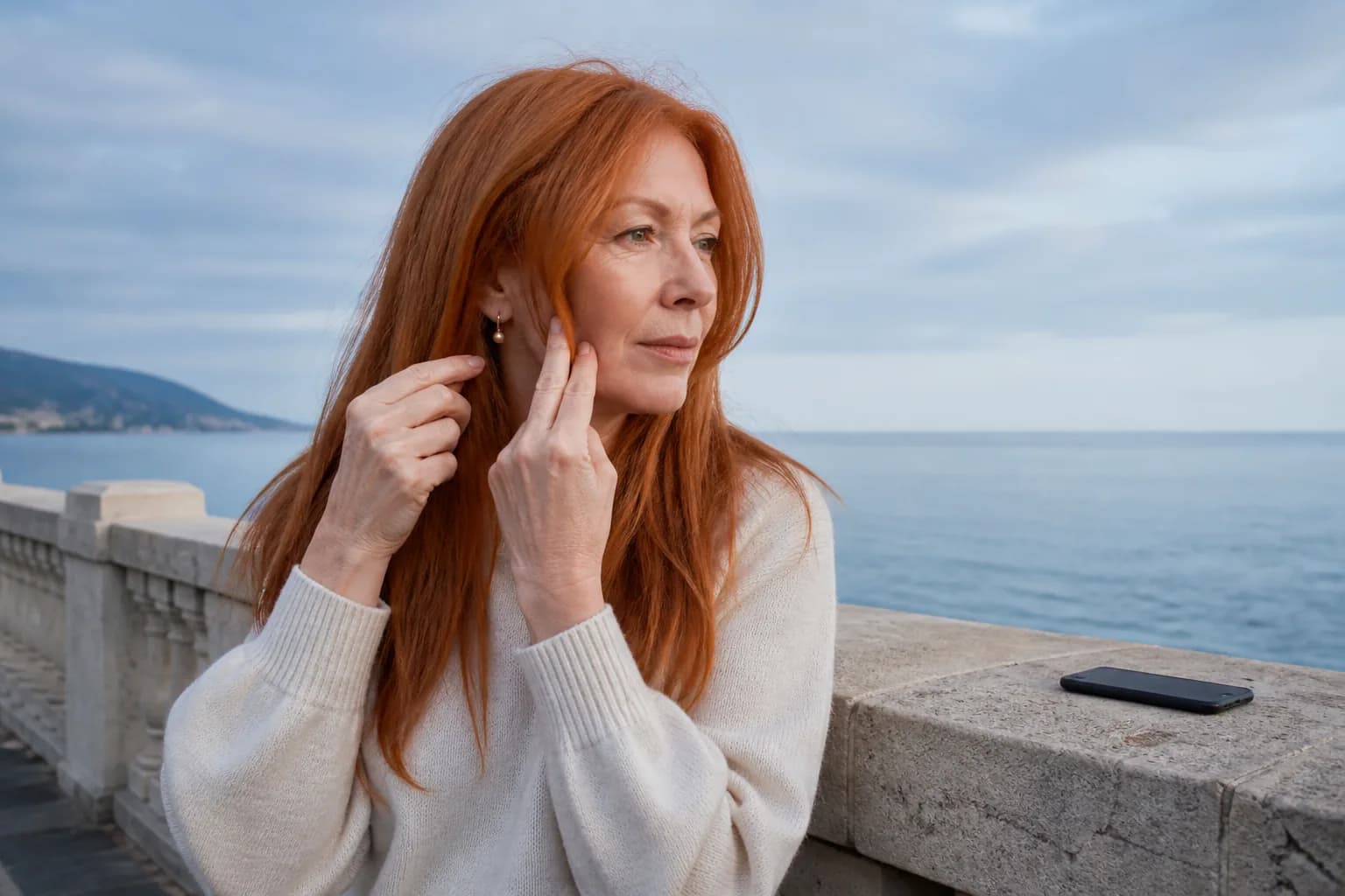 Mature red-haired woman on a seaside promenade indicating where a face-framing layer could begin near her cheekbone