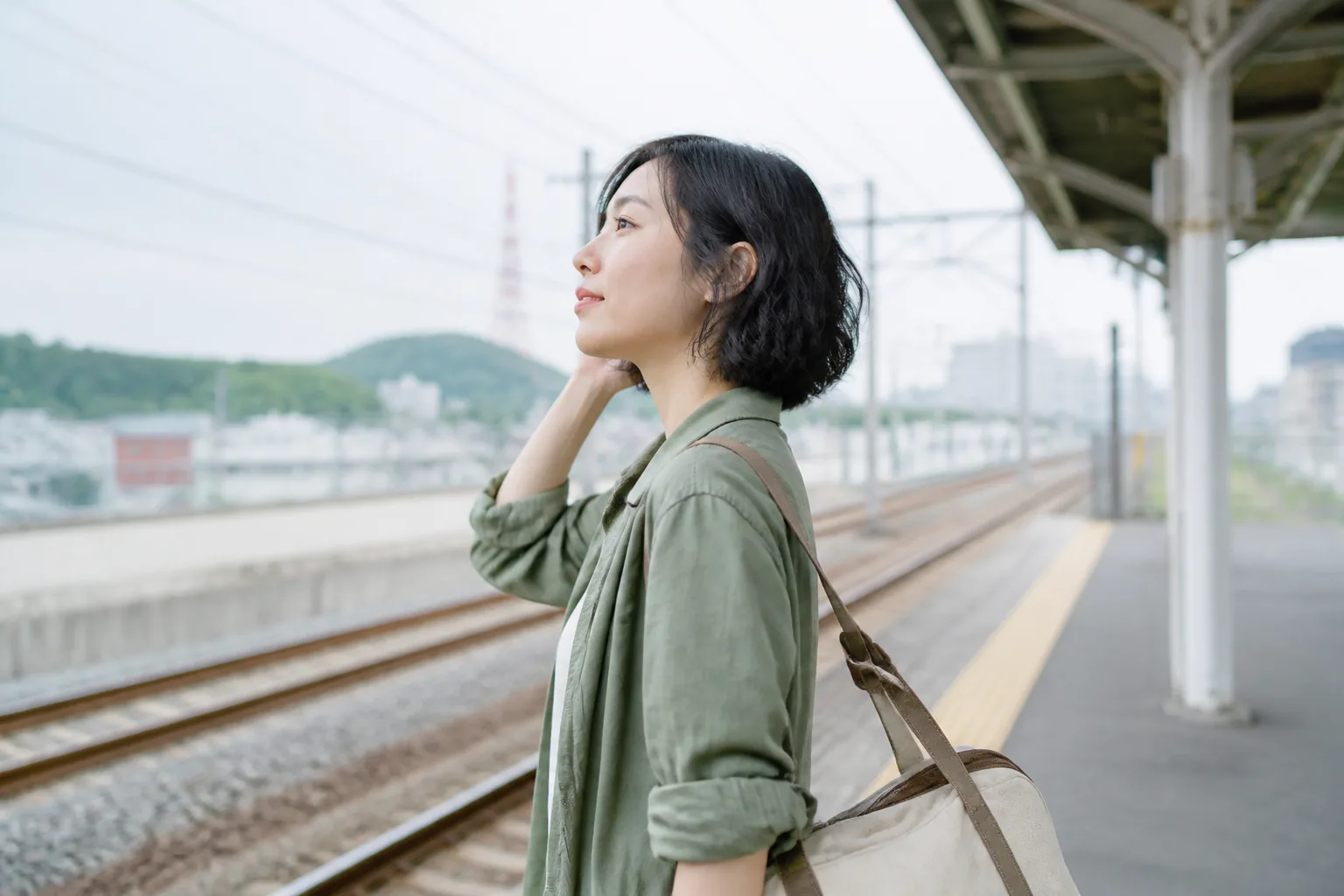 Traveler lightly checks her wavy bob on an outdoor train platform before a trip