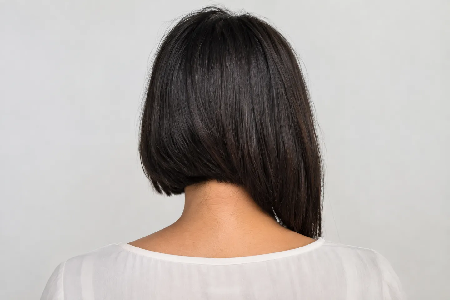Back view of a dark asymmetrical bob connecting a shorter side with a longer section through the rear perimeter