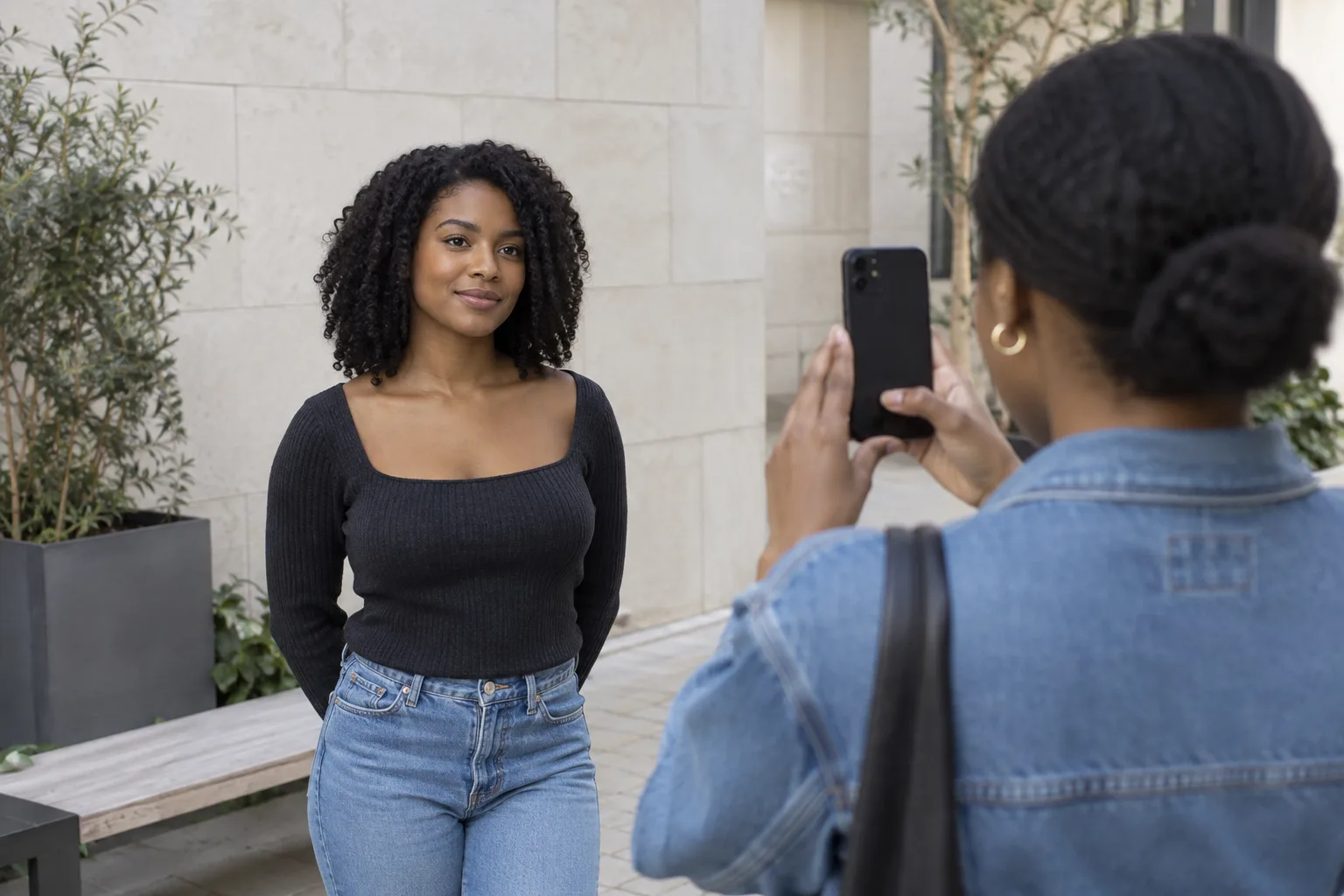 Friend photographing a young woman with dark natural coils at eye level in soft shaded daylight for a consistent hair color preview