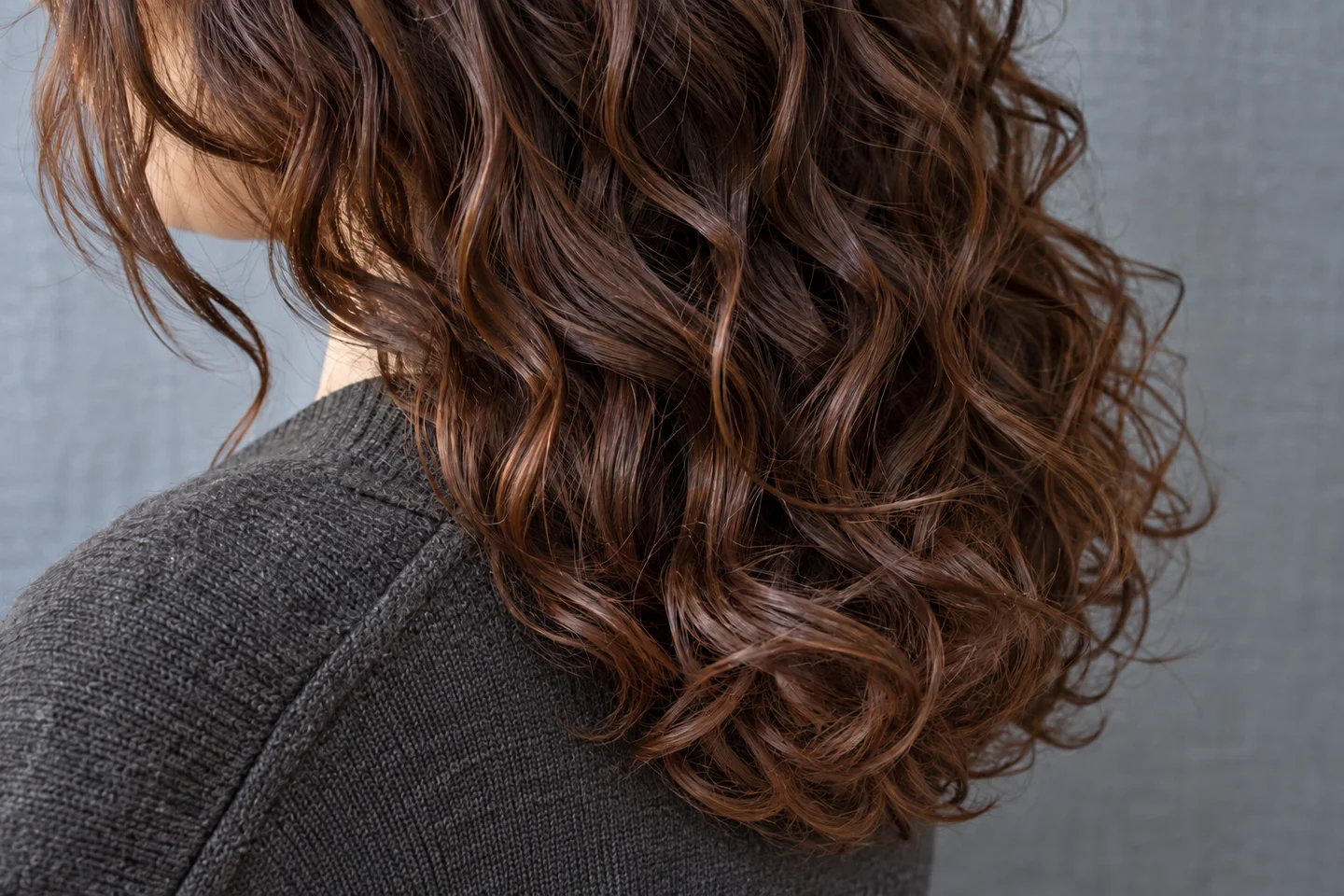 Detalle de ondas caoba secas agrupadas en mechones definidos sobre una prenda gris