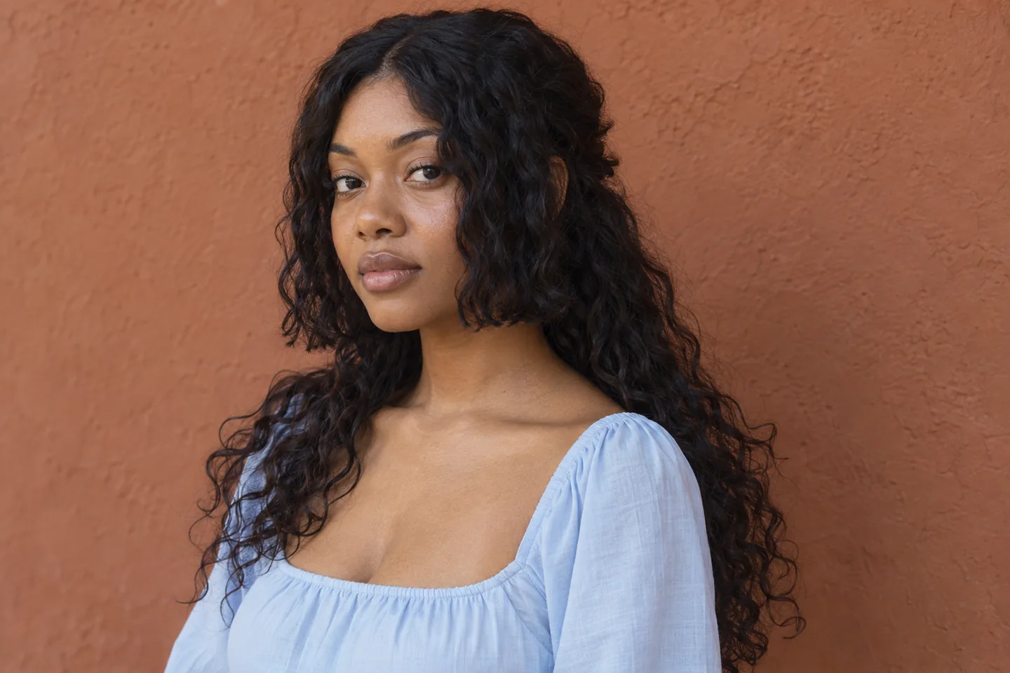 Young Black woman with shorter natural wavy side sections beside her jaw and longer dark hair falling below the shoulders