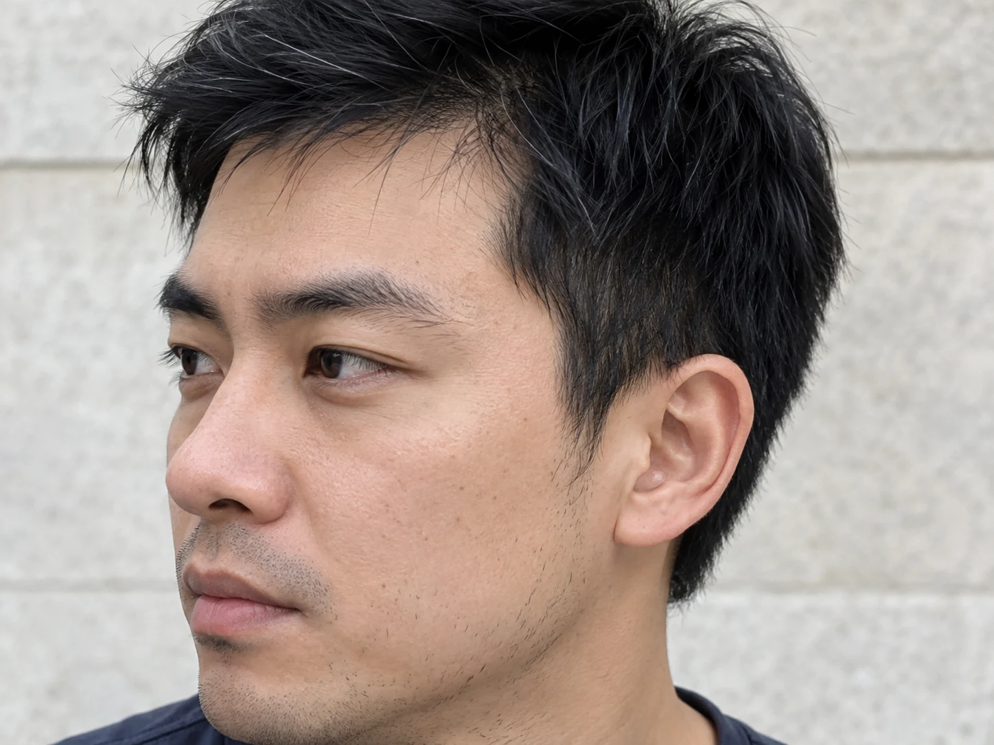 Close three-quarter view of a man's natural temple hairline, individual dark hairs, ear and subtle stubble in soft daylight