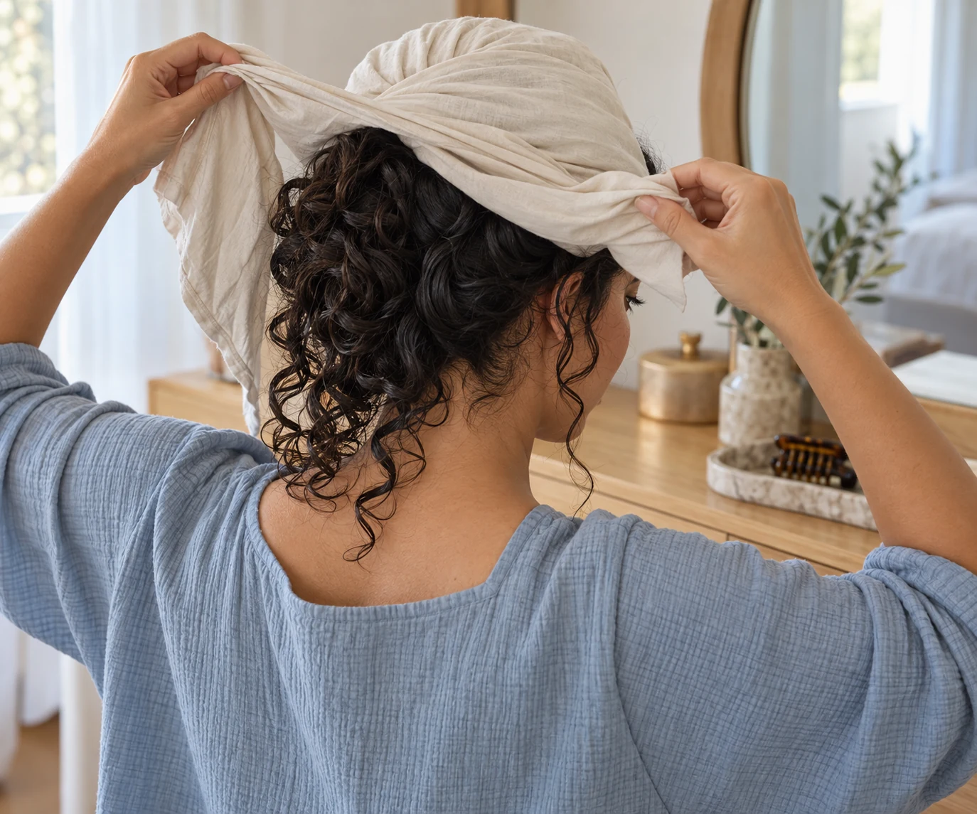 Adult woman opens a slack cream fabric wrap behind her head while damp waves fall freely around the nape