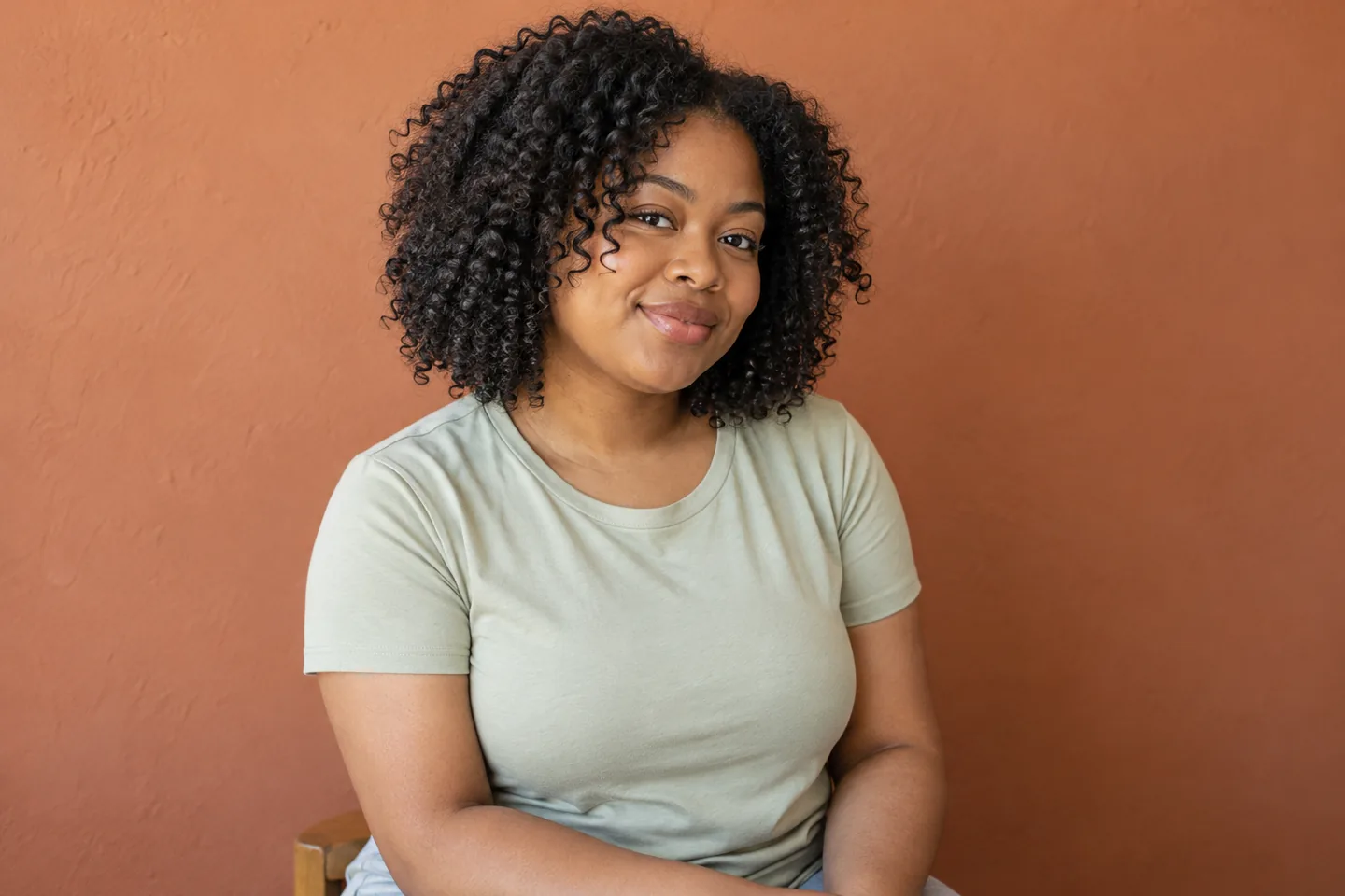 Young woman with a naturally full dry curly bob retaining its rounded side silhouette against a terracotta wall