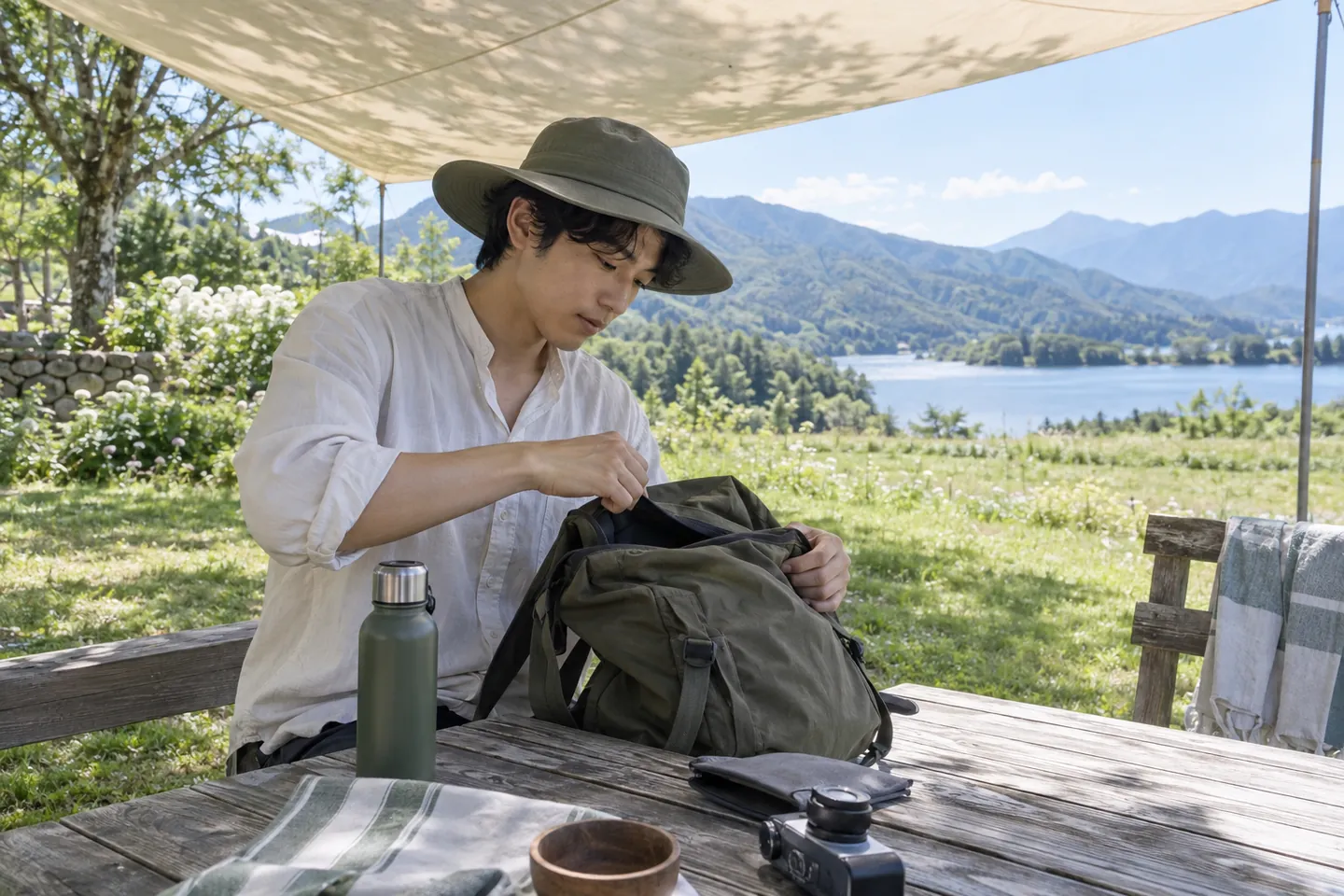 Young man wearing a broad-brim fabric hat organising a day bag beneath a garden shade canopy