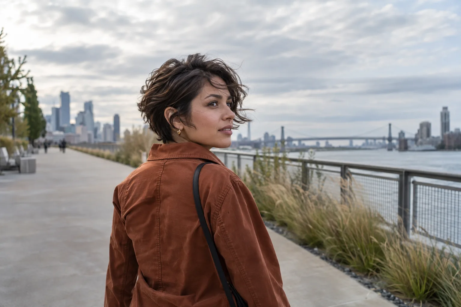 Young woman with a textured bixie walking beside a river while a light breeze reveals the crown, fringe, ears, and nape