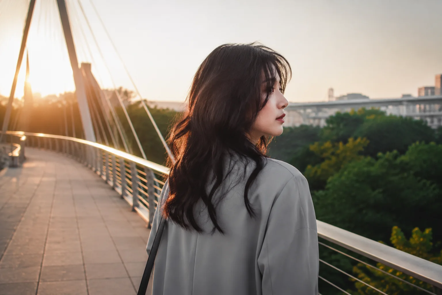 Young woman with long dark layered hair turning on a city footbridge at sunrise to show the moving back silhouette